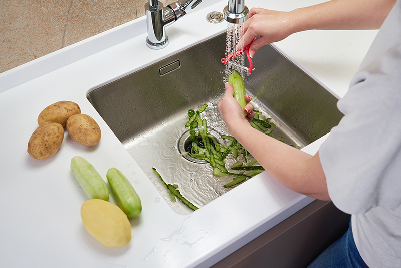 Woman peeling vegetables at kitchen sink with garbage disposal.